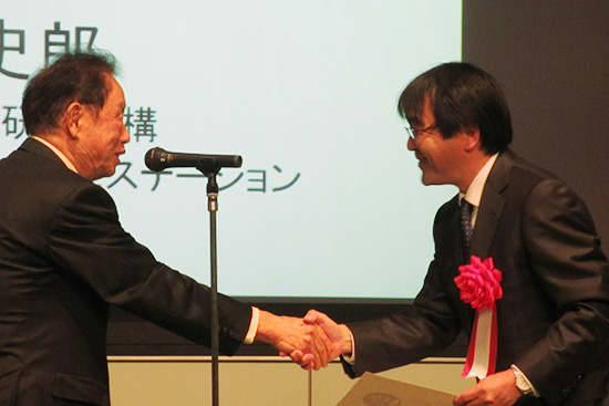 「表彰式で江崎玲於奈氏 (左) と握手を交わす鳥塚ステーション長 (右)」の画像