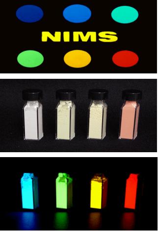 「図上段はNIMSで開発した酸窒化物蛍光体。蛍光体粉末を丸い試料ケースに充填して、365nmの紫外線を照射して撮影したもの。中央のNIMSも黄色蛍光体である。上左 (紫色) および上中央 (青色) は酸窒化物にCe3+添加、上右および下左 (緑色) は酸窒化物にEu2+添加、下中央 (黄色) はα - サイアロンにEu2+添加した蛍光体.下右 (赤色) は今回発表のCaAlSiN3にEu2+を添加した蛍光体。図中、下段はNIMSで開発した蛍光体粉末。」の画像